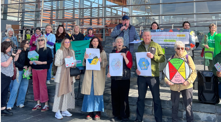 A group of people stand outside the Senedd. They are holding posters and banners.